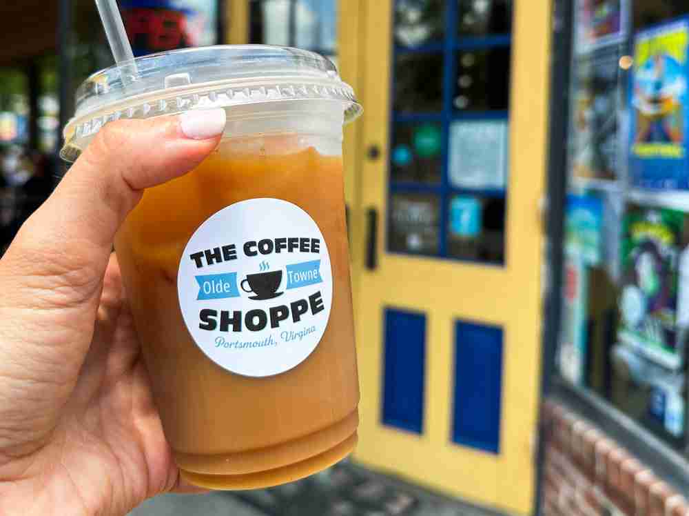 a girl holds up a to-go cup filled with iced coffee