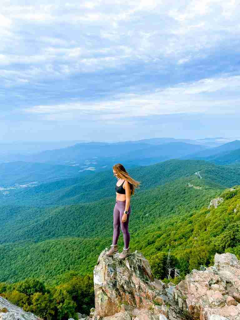 girl on a hike stands on the edge of a mountain